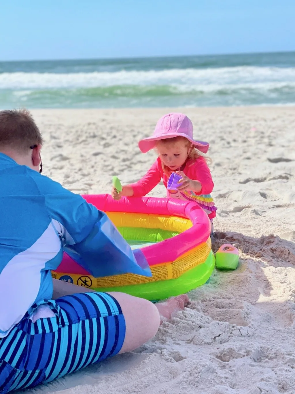 two kids playing with an inflatable pool at the beach