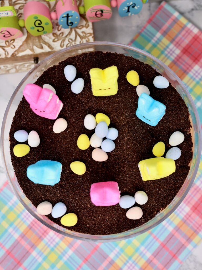 dirt cake for easter in a glass trifle bowl with marshmallow peeps and cadbury mini eggs on top