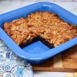 sliced pecan pie brownies in a blue baking dish on top of a wood cutting board with a blue and white patterned napkin