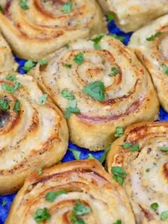 ham and swiss cheese crescent pinwheels in a bright blue baking dish sprinkled with parsley on the top