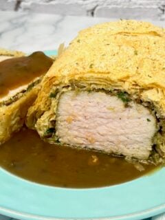 a pork tenderloin wrapped in phyllo dough and sitting on a plate with brown gravy