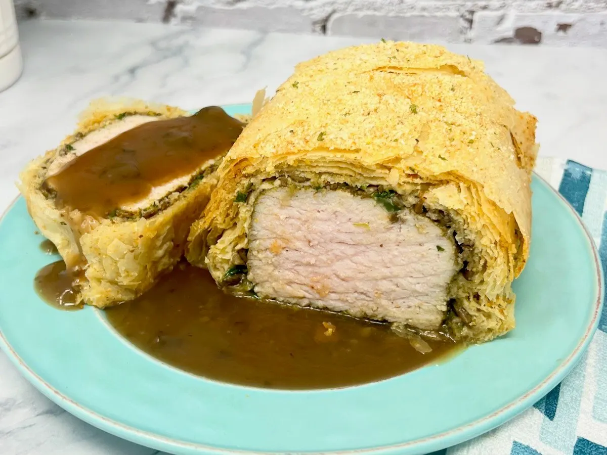 a pork tenderloin wrapped in phyllo dough and sitting on a plate with brown gravy