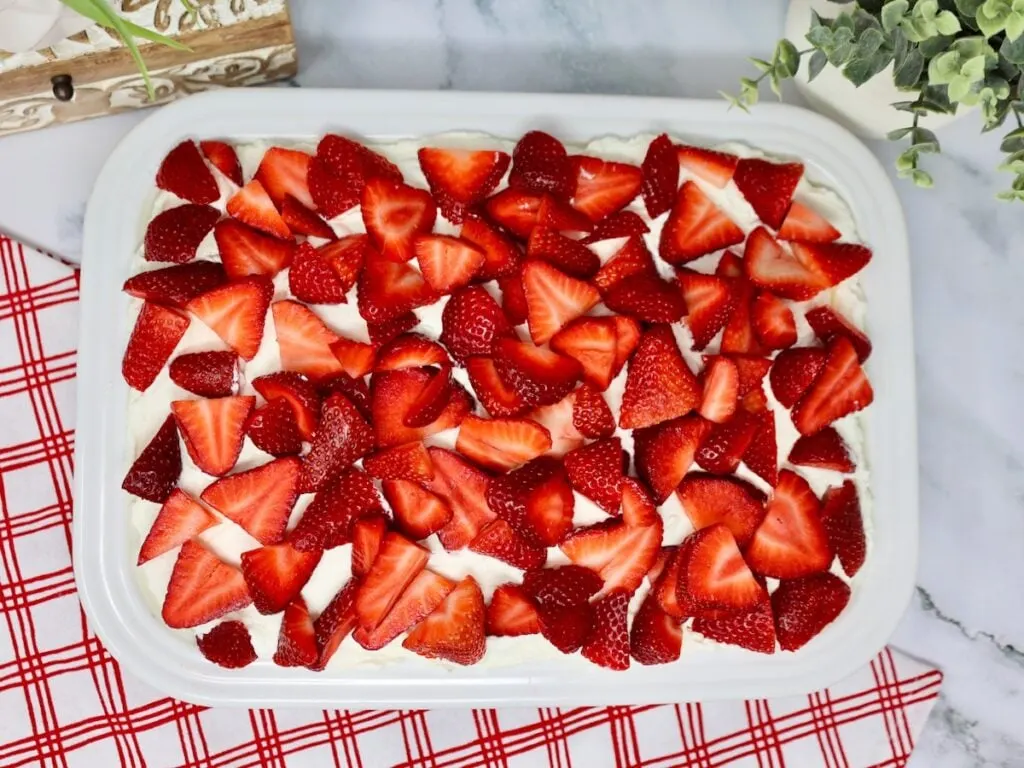 white baking dish with a strawberry cream cake in it, you can see strawberries