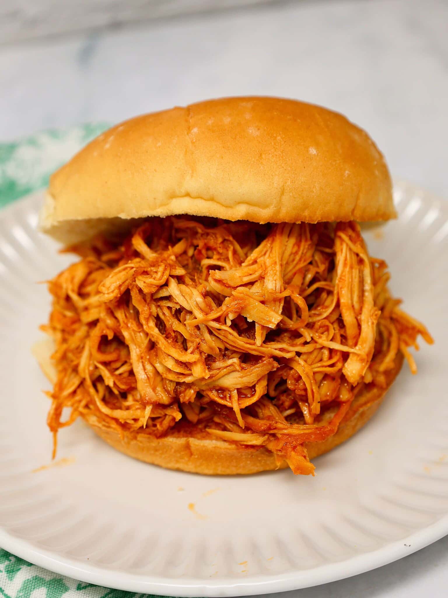 Easy crockpot BBQ chicken piled on a bun with barbecue sauce