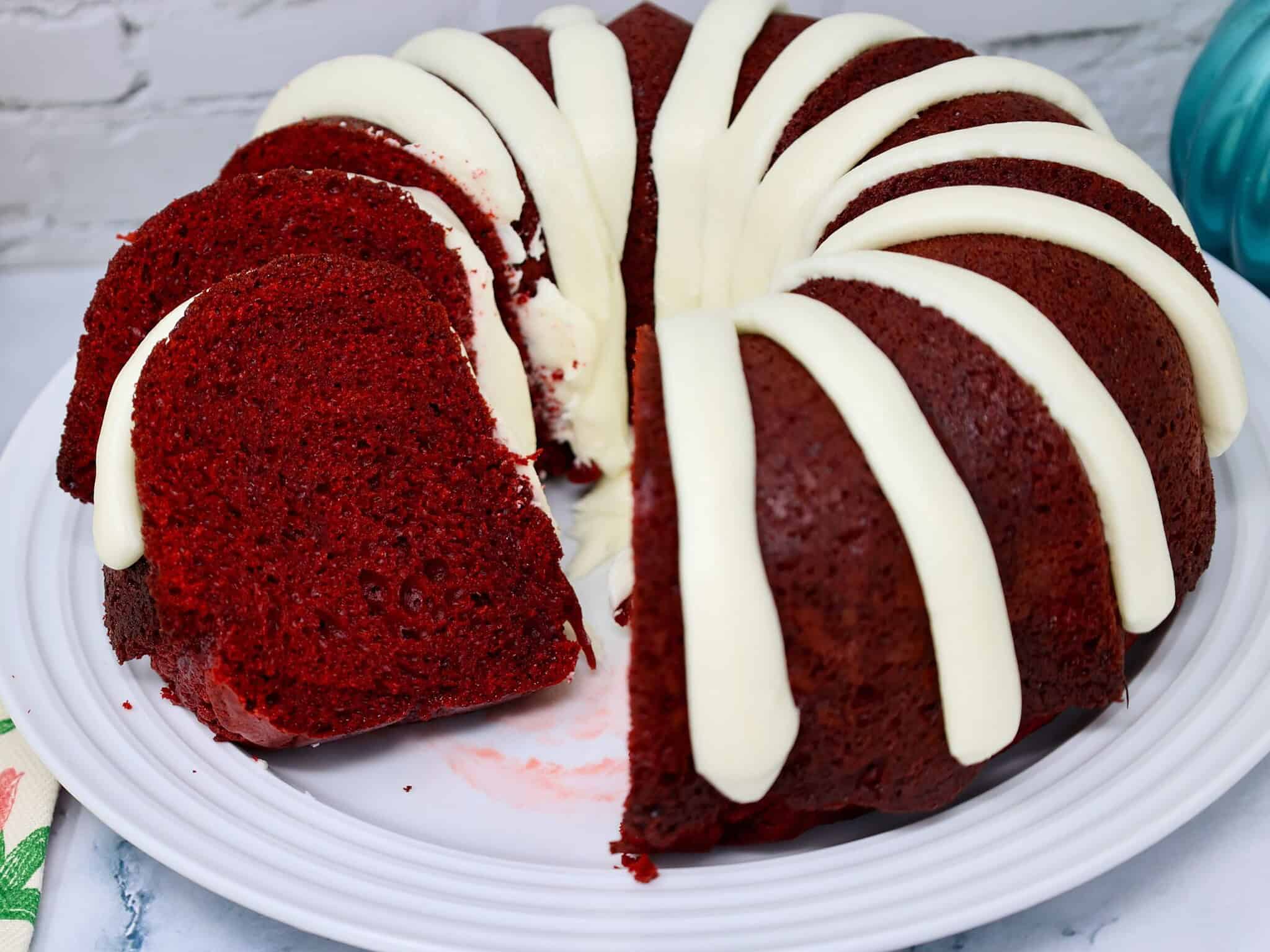 Close-up of soft red velvet cake slice with creamy frosting drizzle