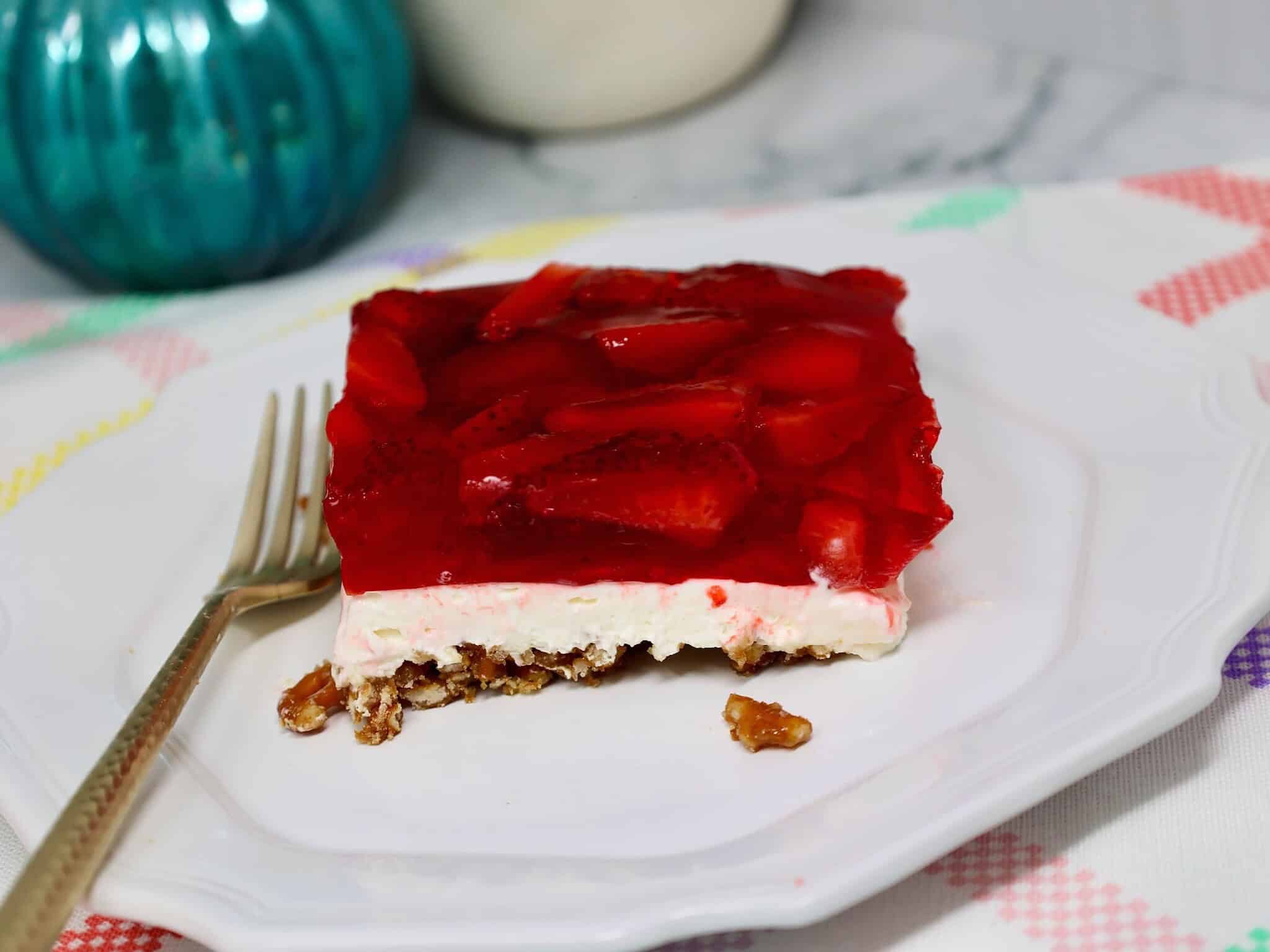 Spoon scooping strawberry pretzel salad showing soft cream layer and crunchy pretzel crust texture