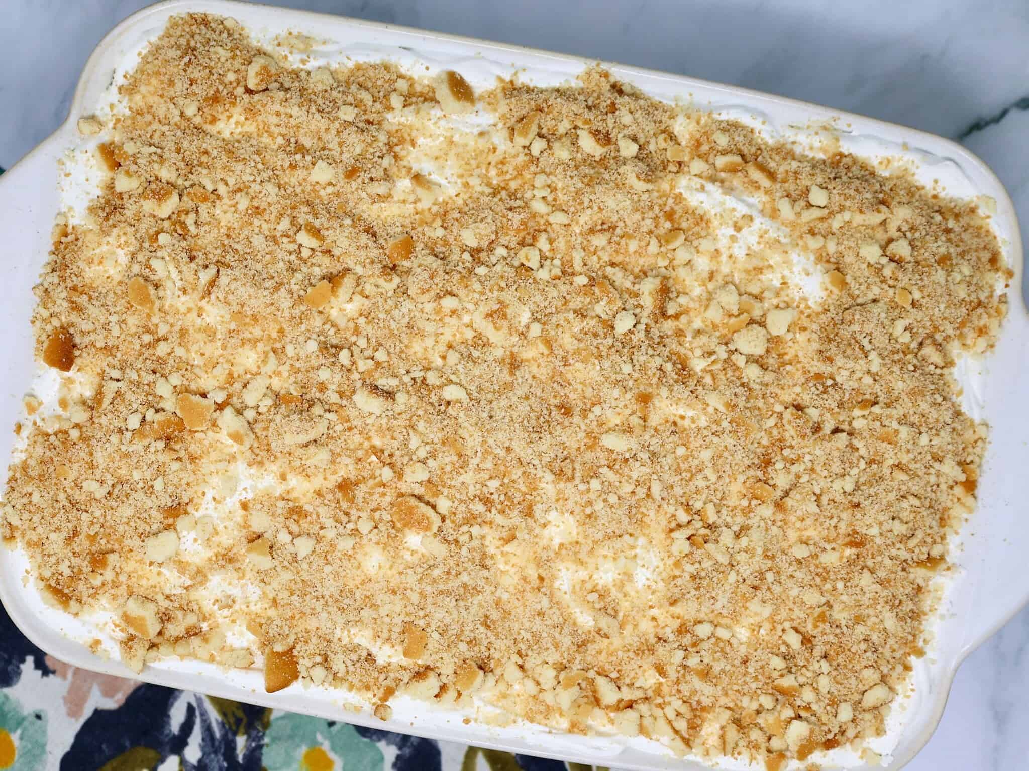A 9x13 baking dish of Banana Pudding Poke Cake topped with fluffy whipped topping and crushed vanilla wafers.