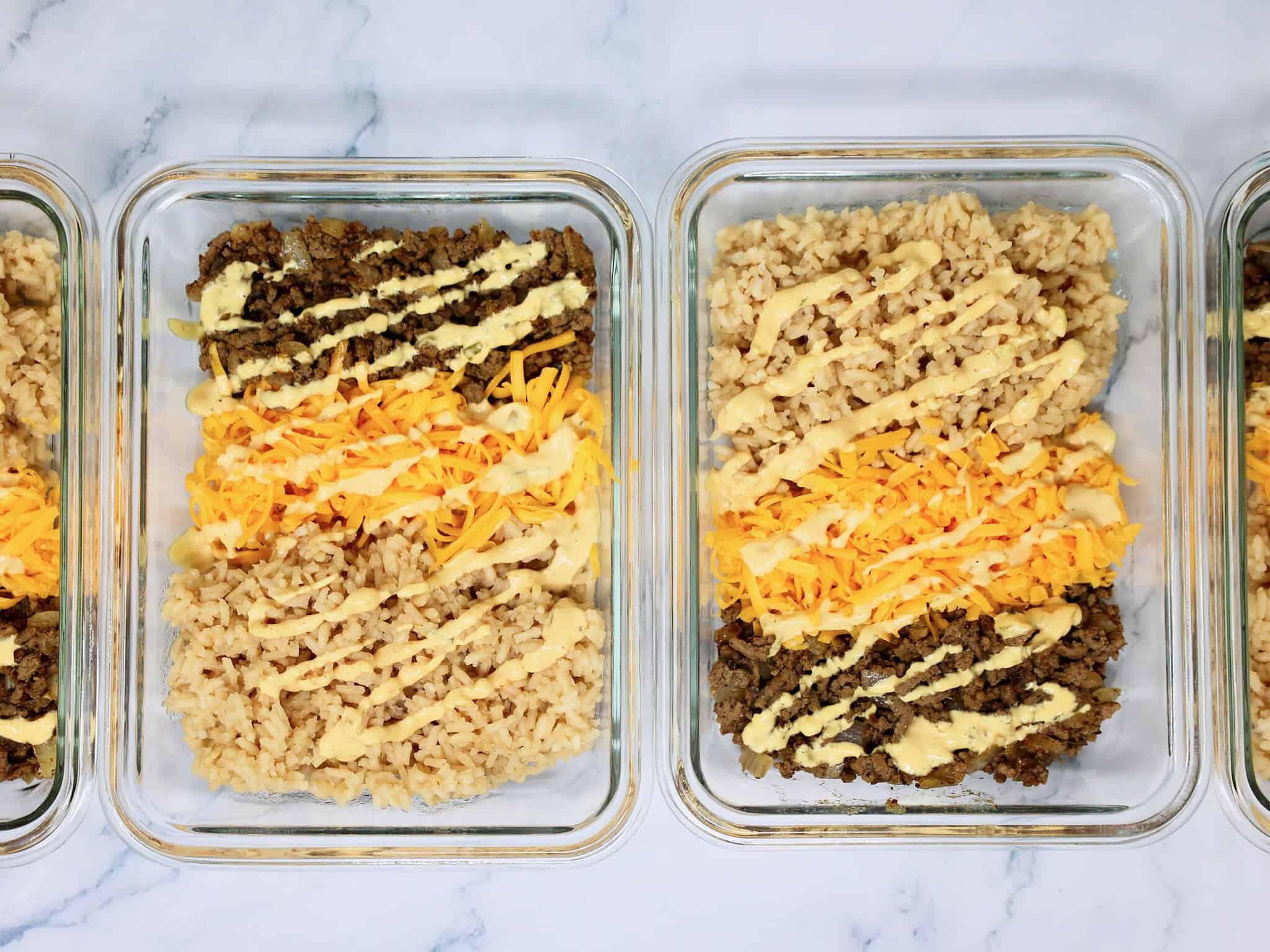 Meal prep Cheeseburger Rice Bowls in containers with beef, rice, cheese, and burger toppings