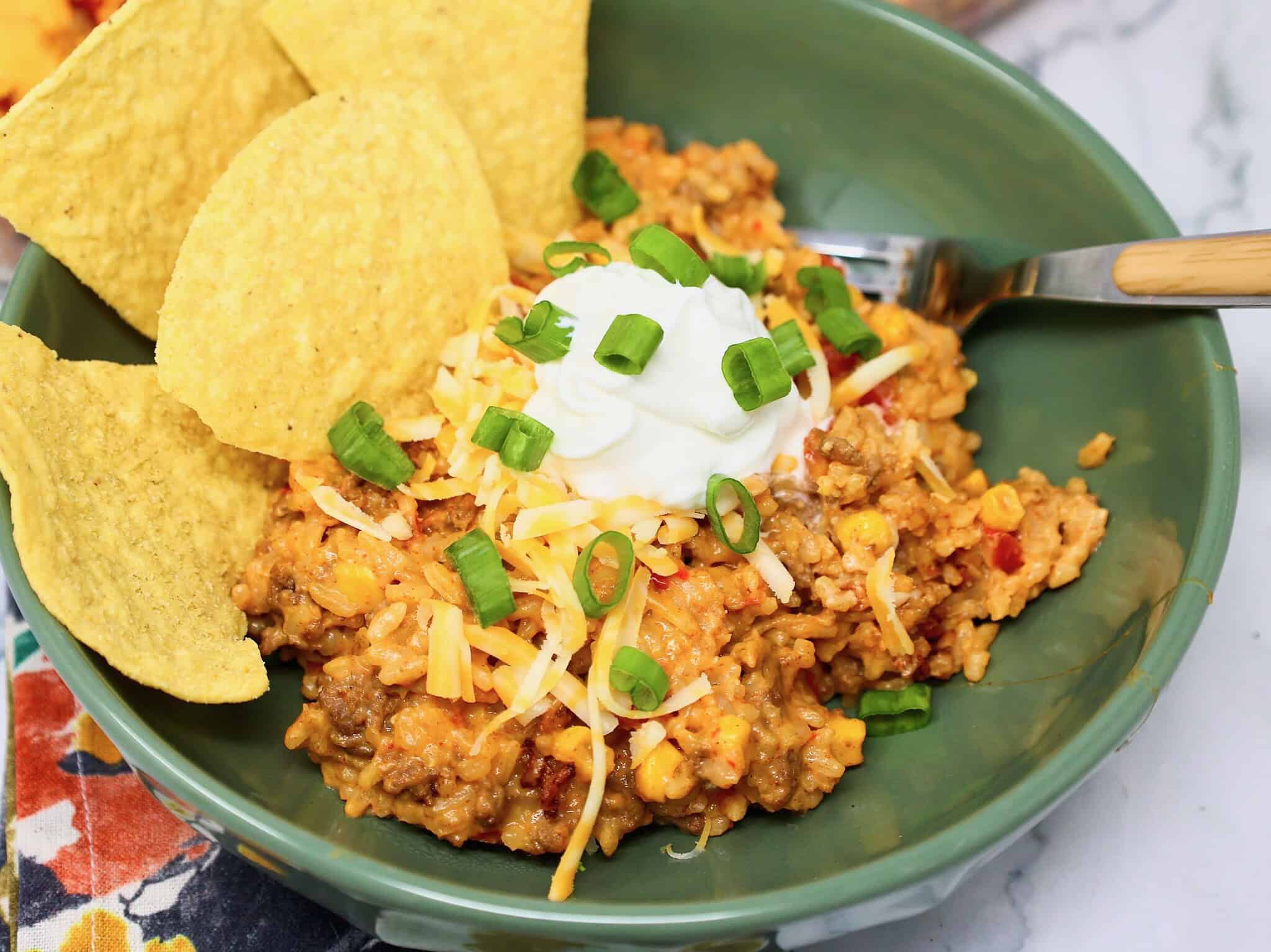 Cheesy beef and rice bowl topped with sour cream, green onions and tortilla chips