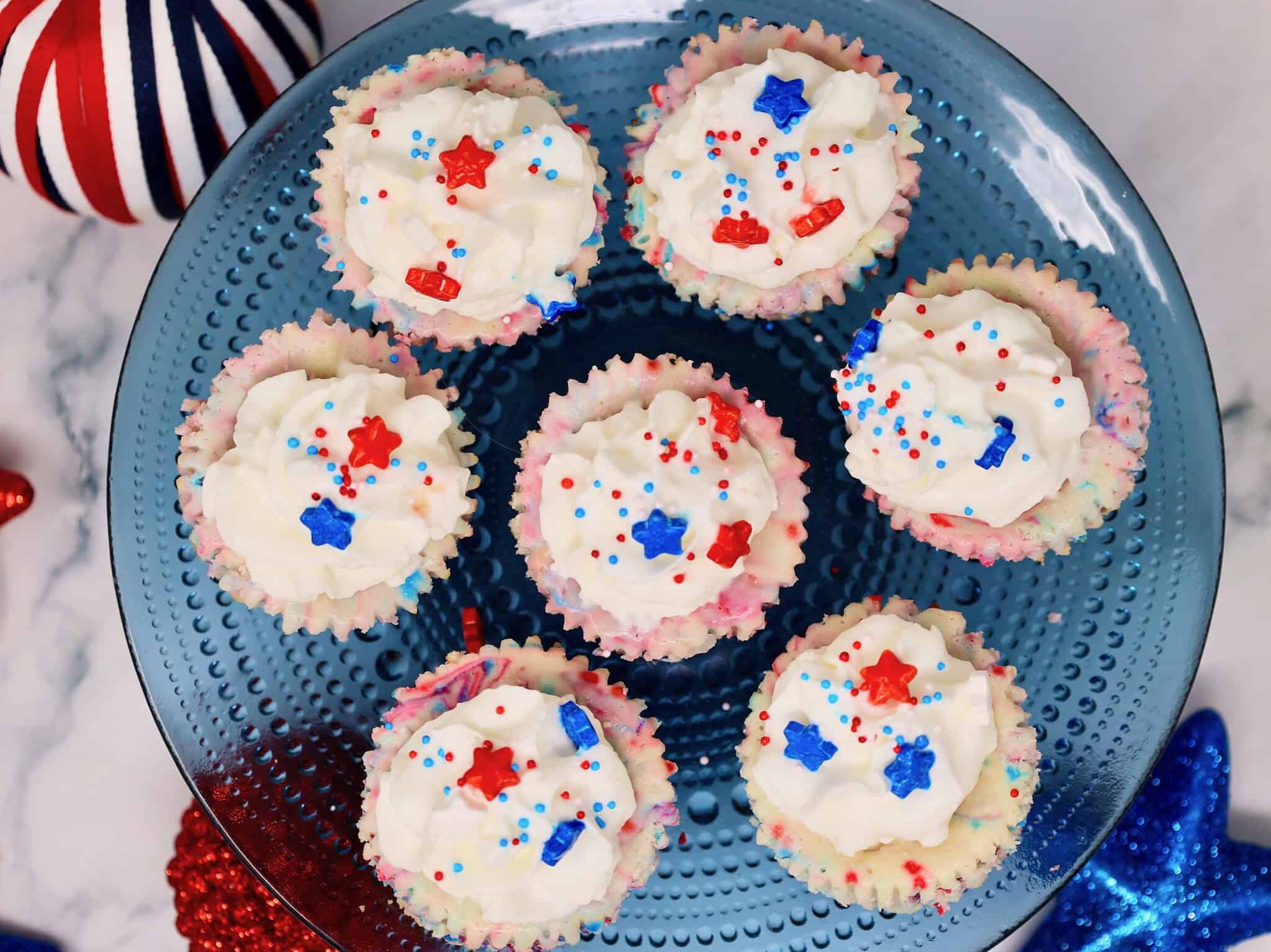 Red white and blue mini cheesecakes topped with whipped cream and fresh berries for a 4th of July dessert