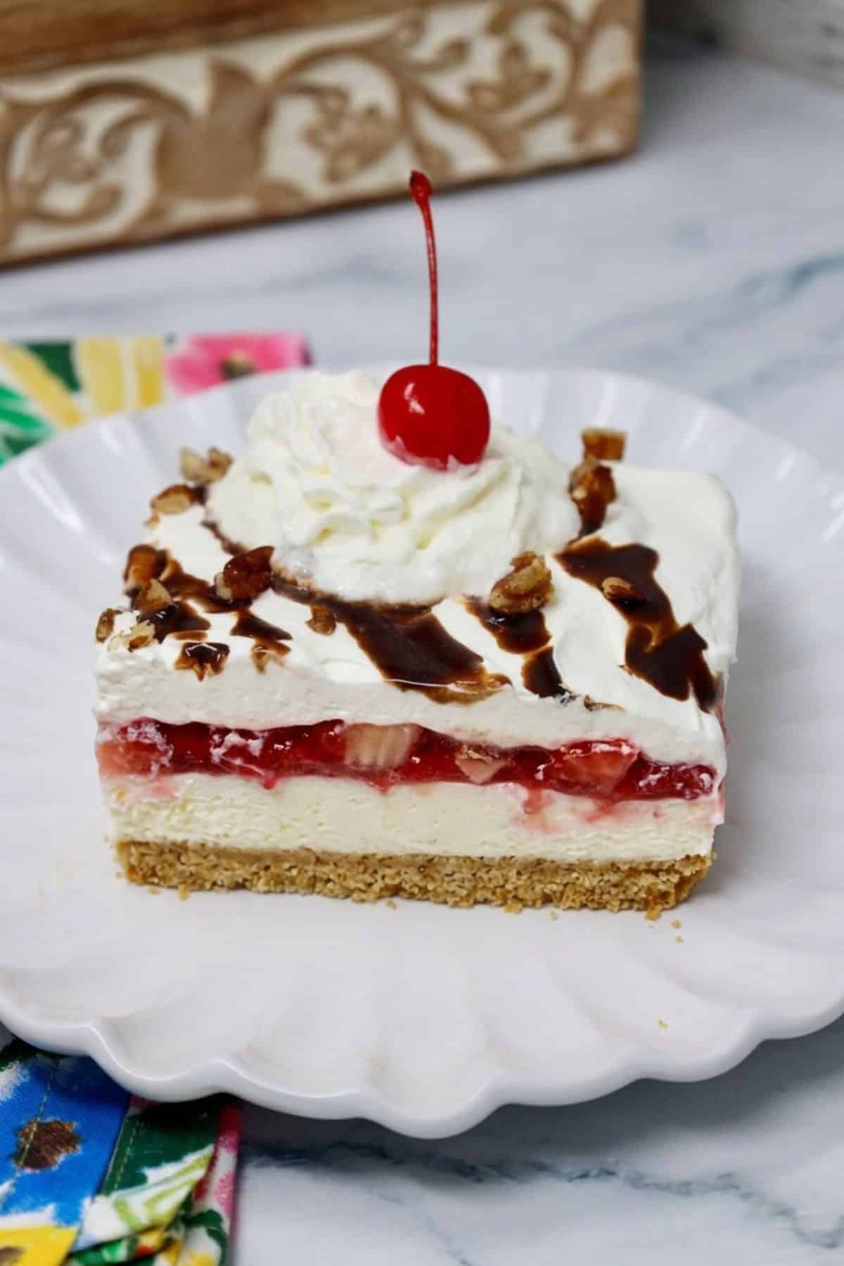 Slice of no bake banana split dessert with graham cracker crust, cream cheese filling, bananas, and strawberries