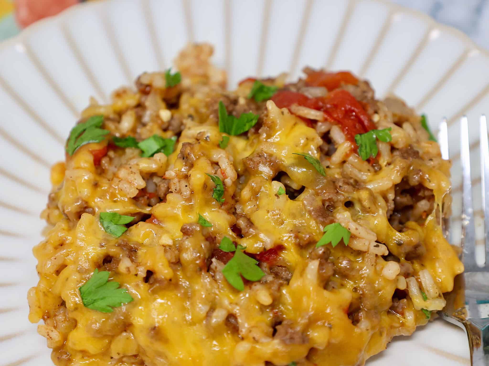 Close view of melted cheddar over seasoned ground beef, rice, and tomatoes