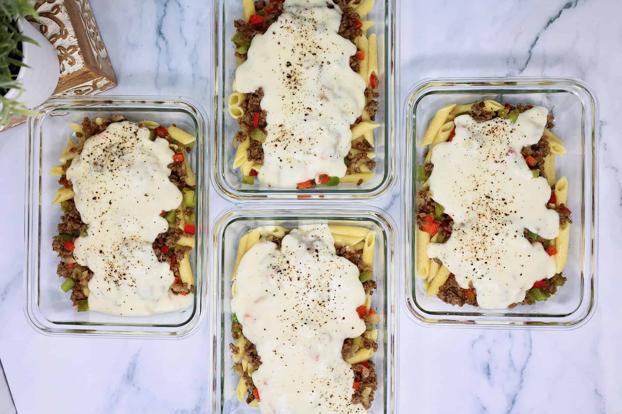 Four meal prep containers filled with Philly cheesesteak pasta, ground beef, and vegetables