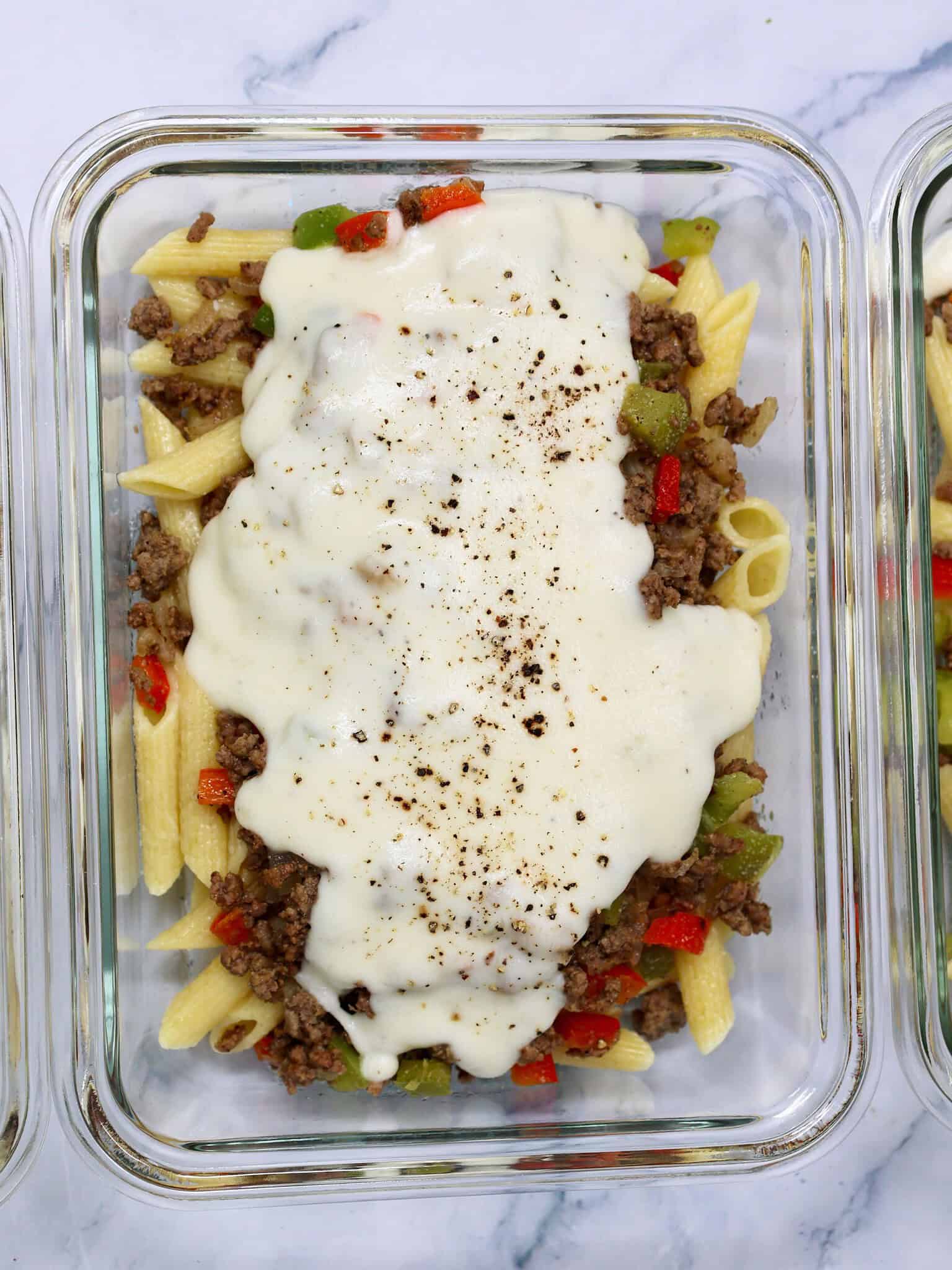 Close view of penne pasta topped with ground beef, sautéed peppers, onions, and provolone sauce