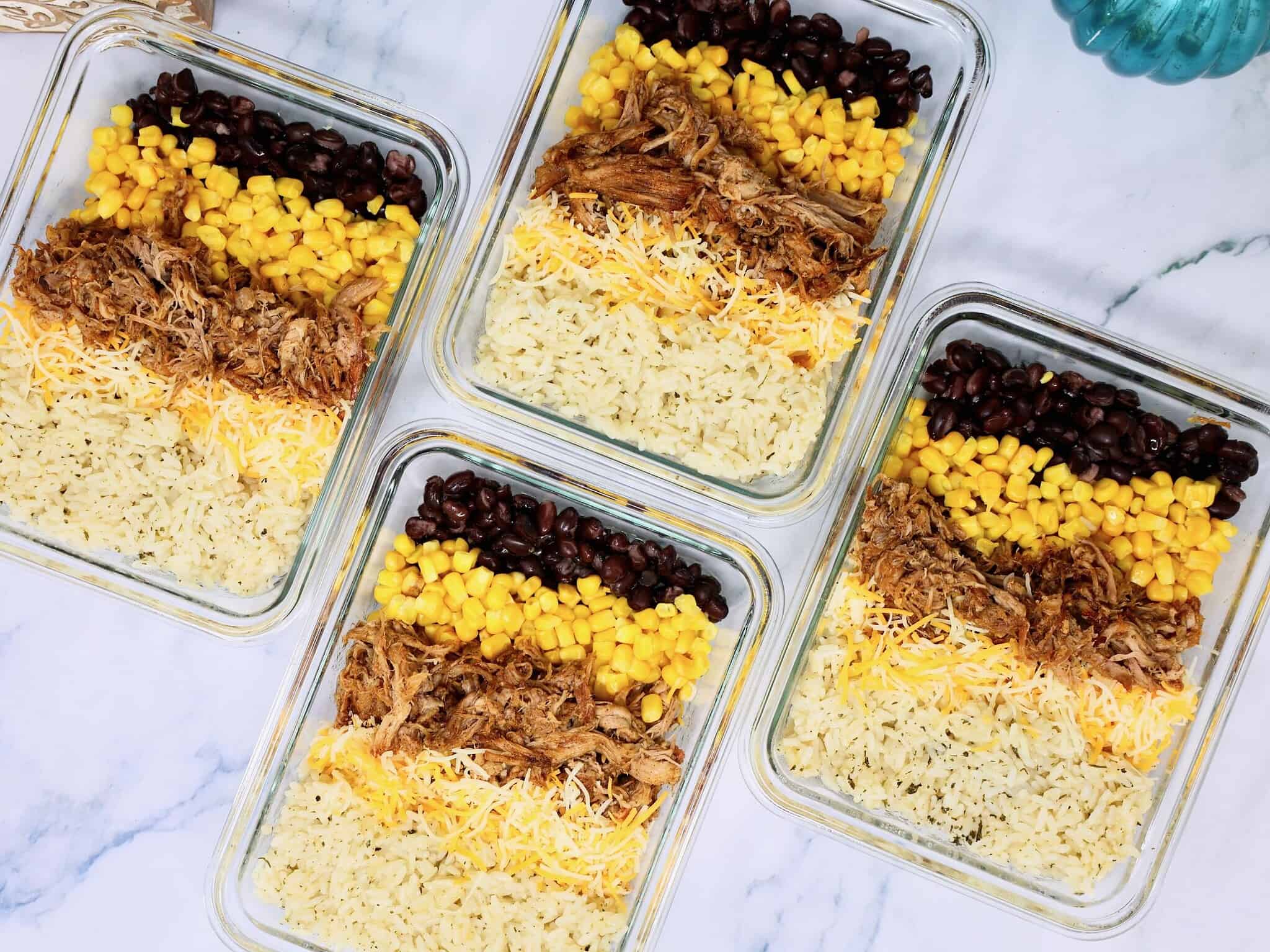 Four pulled pork burrito bowls portioned into individual meal prep containers
