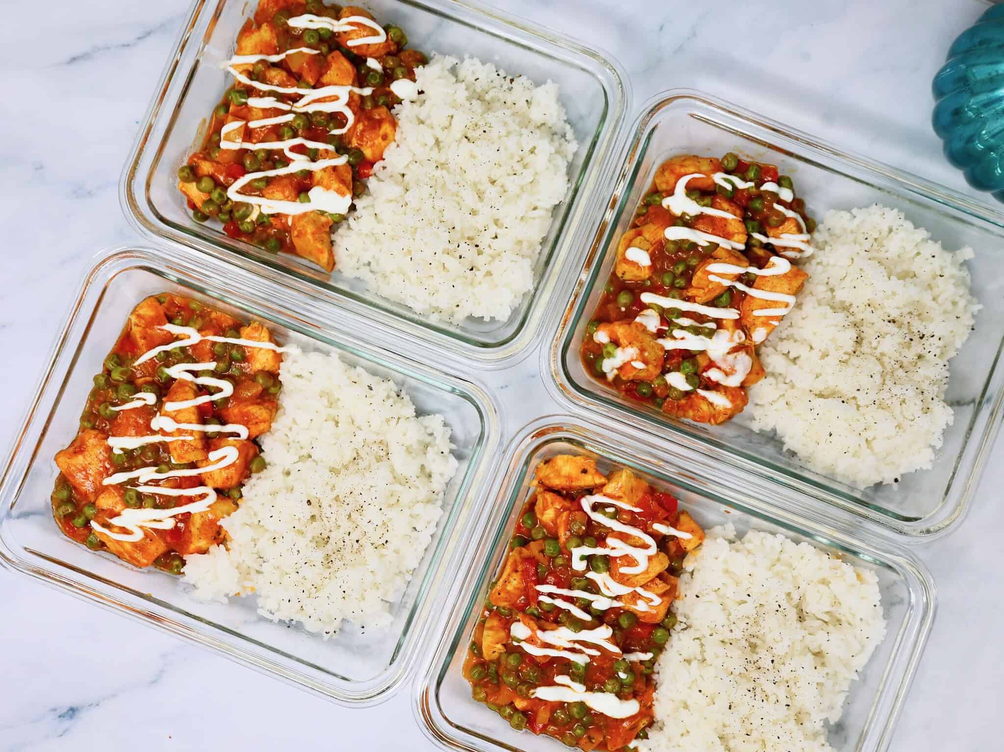 Chicken tikka masala bowl topped with plain Greek yogurt in meal prep containers