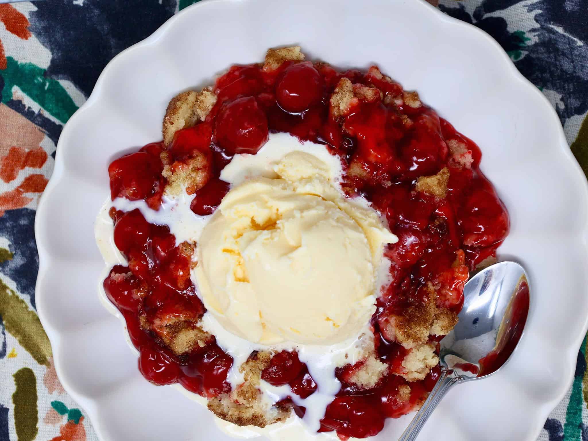 Warm cherry crisp topped with a scoop of vanilla ice cream melting over the cinnamon sugar cookie crust.